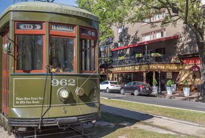 A green streetcar is parked on a city street with buildings and trees in the background.